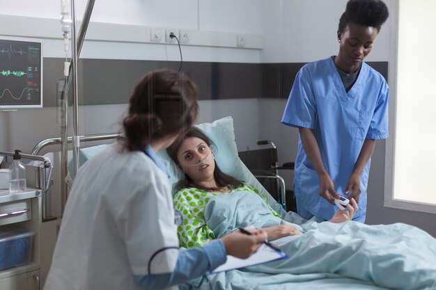 Assisstant afro-americano coloca oxímetro no dedo para verificar o pulso de batimento cardíaco durante a consulta de recuperação ...