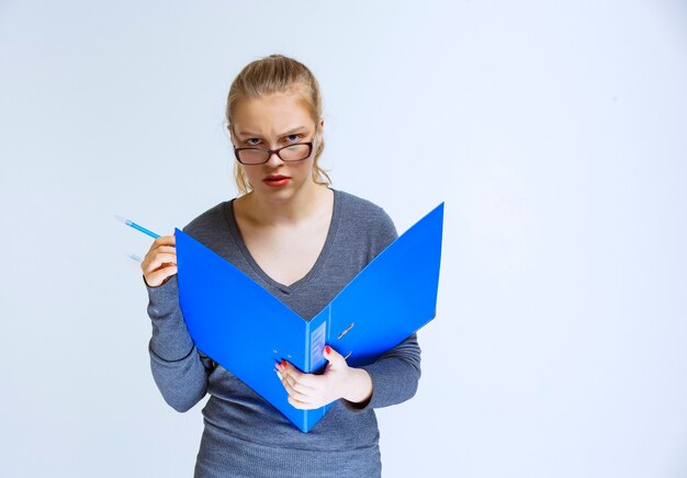 Assistente com óculos verificando a pasta azul e parece pensativo e confuso.