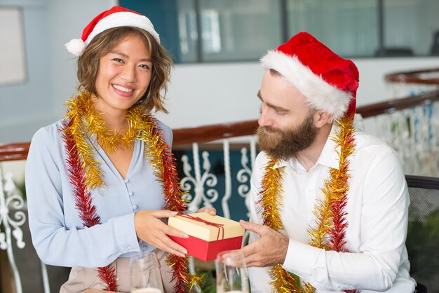 Assistente de escritório alegre no chapéu de Papai Noel dando presente de Natal