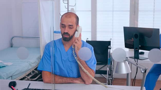 Assistente falando no telefone, verificando a nomeação, enquanto a mulher que trabalha no pc sentada no hospital. médico em uniforme de medicina, escrevendo a lista de pacientes consultados e diagnosticados, fazendo pesquisas.