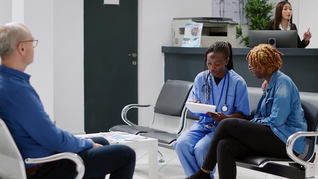 Assistente médico fazendo consulta com o paciente no saguão da recepção do hospital, sentado na sala de espera e falando sobre saúde ou tratamento. enfermeira dando conselhos ao jovem adulto.