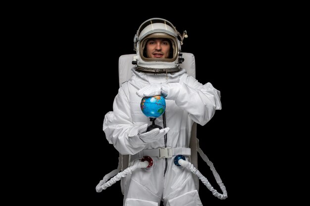 Astronauta do dia do astronauta em traje espacial em branco sorrindo capacete de vidro aberto segurando e girando globus