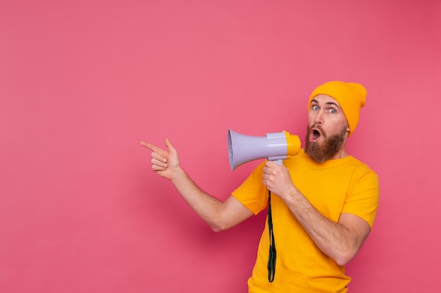 Atenção! homem europeu com megafone apontando o dedo para a esquerda em fundo rosa