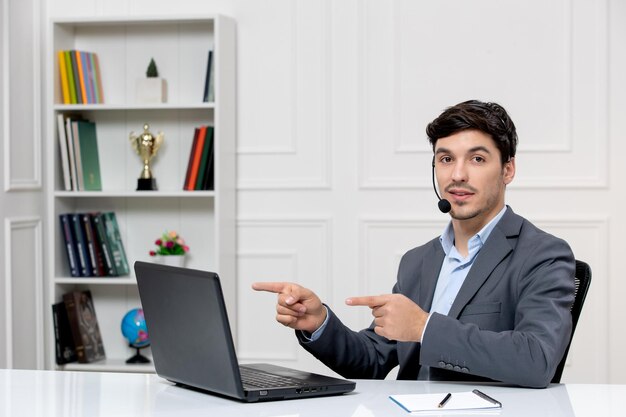 Atendimento ao cliente bonitinho de terno cinza com computador e fone de ouvido sorrindo