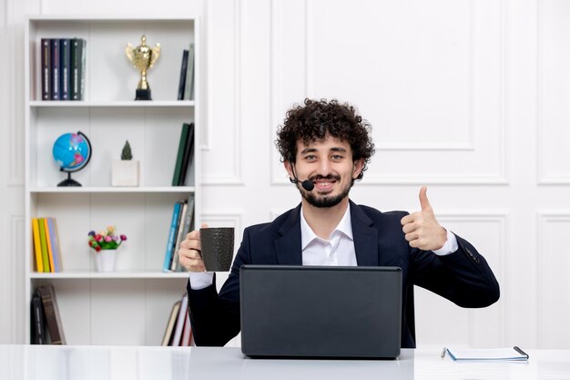 Atendimento ao cliente bonito homem encaracolado em terno de escritório com computador e fone de ouvido feliz por um café