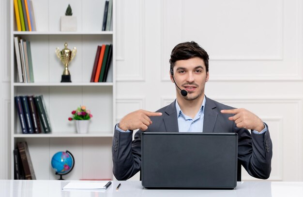 Atendimento ao cliente homem bonito de terno cinza com computador e fone de ouvido apontando para si mesmo