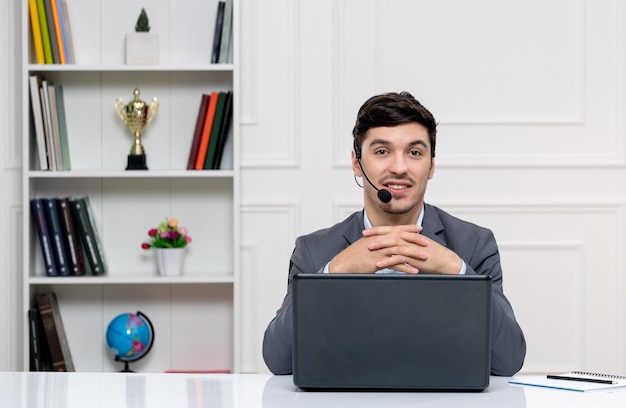 Atendimento ao cliente homem bonito de terno cinza com computador e fone de ouvido cruzando as mãos