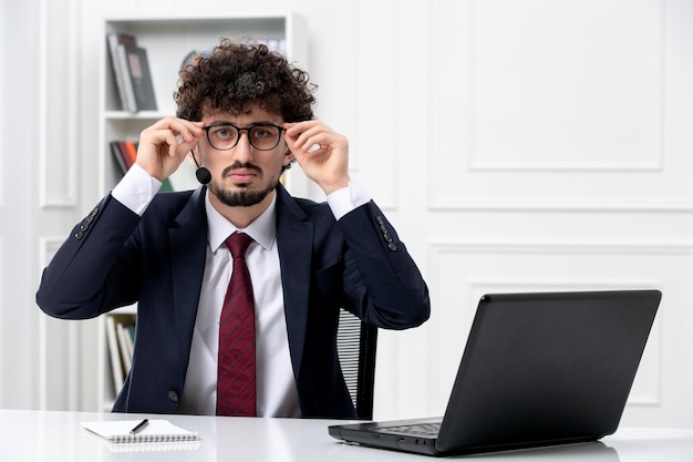 Atendimento ao cliente jovem bonito em terno de escritório com laptop e fone de ouvido colocando óculos