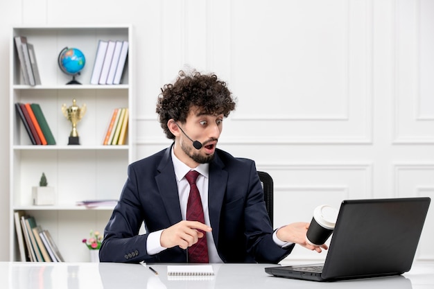 Atendimento ao cliente jovem bonito em terno de escritório com laptop e fone de ouvido derramando café