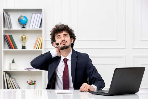 Atendimento ao cliente jovem bonito em terno de escritório com laptop e fone de ouvido tocando o pescoço e cansado