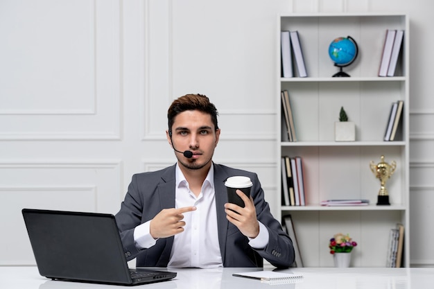 Atendimento ao cliente muito cavalheiro com computador em terno de escritório cinza segurando o copo de papel preto