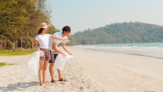 Ativistas felizes novos asiáticos da família que recolhem resíduos plásticos na praia. Os voluntários da Ásia ajudam a manter a natureza limpa e a recolher o lixo. Conceito sobre problemas de poluição de conservação ambiental.