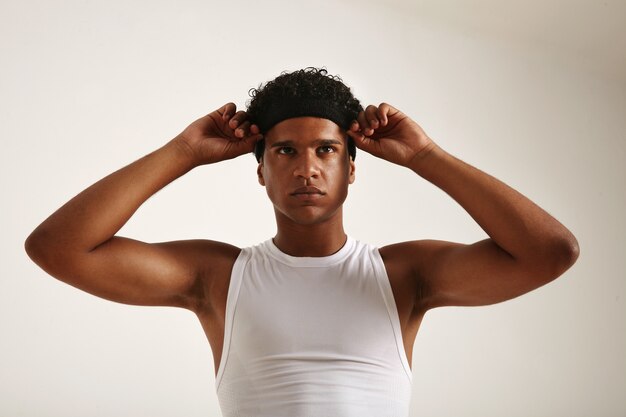 Atleta afro-americano musculoso com camisa de basquete branca ajustando a faixa preta na cabeça e parecendo ligeiramente