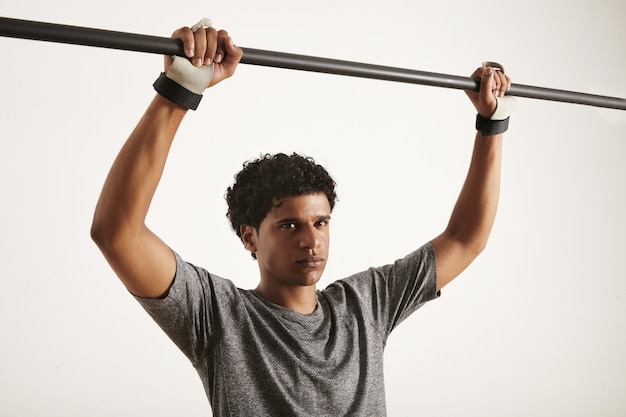 Atleta afro-americano vestindo camiseta técnica e proteção para as mãos de cross fitness segurando barra pullup de carbono isolada no branco