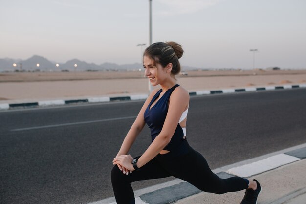 Atleta alegre ativa, alongamento na estrada. País tropical, sorridente, alegre, motivação, exercício, estilo de vida saudável.