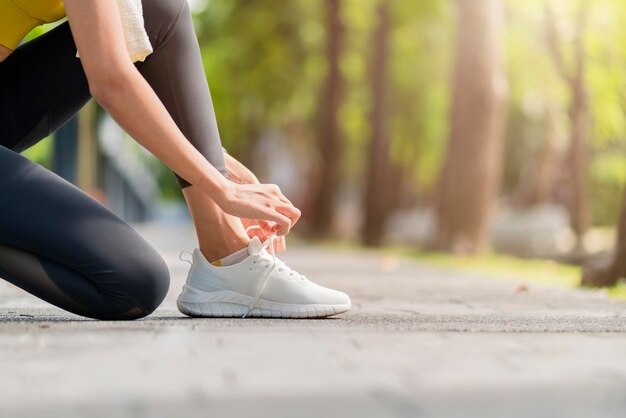 Atleta asiática do esporte feminino amarrando cadarços para correr na estrada no parque tênis de corrida no parque público Mulher asiática ativa amarrando o cadarço antes de correr mulher amarrando os cadarços