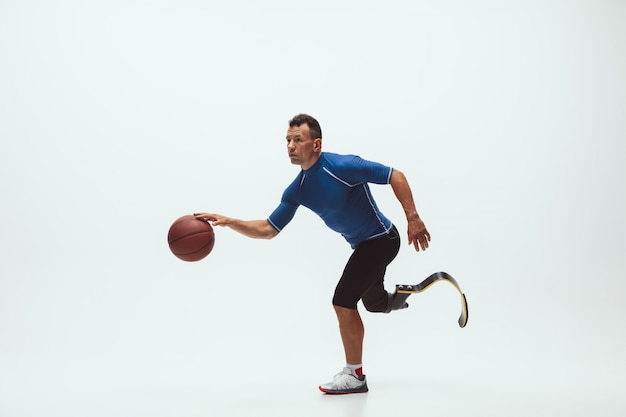 Atleta com deficiência ou amputado isolado no espaço branco do estúdio. Jogador profissional de basquete masculino com prótese de perna treinando e praticando em estúdio.