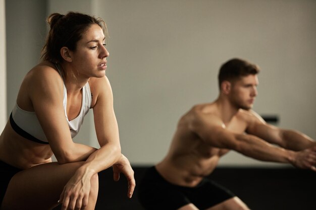 Atleta exausta descansando durante o treinamento cruzado em uma academia Há um homem malhando no fundo