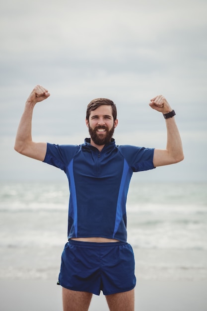 Atleta feliz em pé na praia com as mãos levantadas