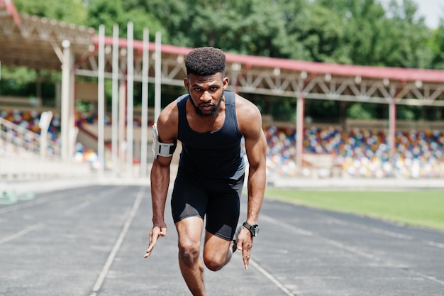 Atleta masculino americano africano em roupas esportivas correndo sozinho em uma pista de corrida no estádio