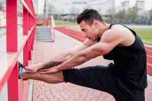 Foto grátis atleta masculino jovem fitness, esticando a perna no estádio