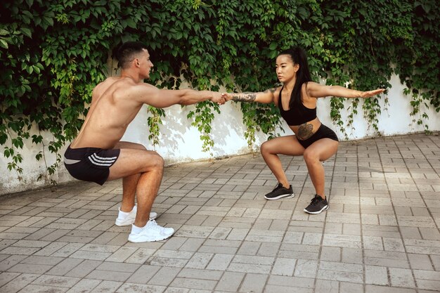 Atletas musculosos fazendo exercícios no parque. Ginástica, treino, flexibilidade de treino de fitness. Cidade de verão em um dia ensolarado no campo de fundo. Estilo de vida ativo e saudável, juventude, musculação.