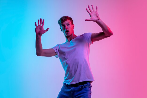 Atônito. Retrato de jovem caucasiano em fundo gradiente estúdio azul-rosa em luz de néon. Conceito de juventude, emoções humanas, expressão facial, vendas, anúncio. Bela modelo em casual.