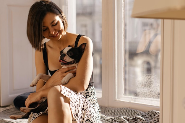 Foto grátis atraente jovem anfitriã caucasiana e cachorro estão sentados juntos no peitoril da janela dentro de casa conceito de vida real em casa doce