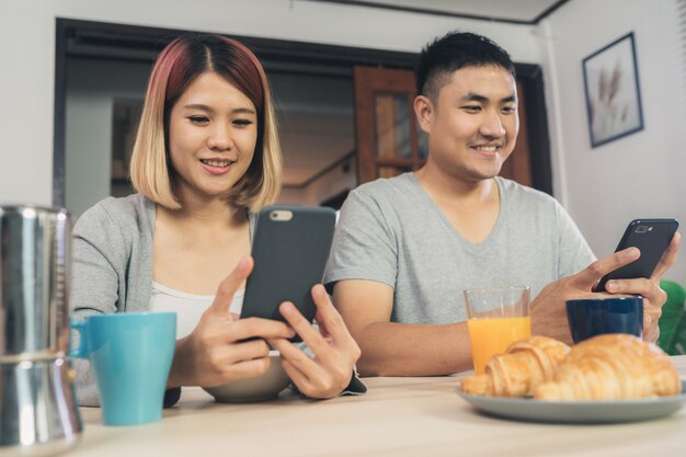 Atraente jovem casal asiático distraído na mesa com jornal e telefone celular