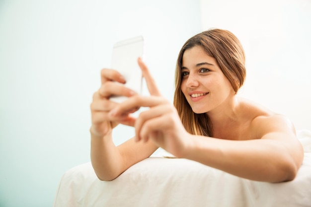 Atraente jovem morena tirando uma selfie com seu smartphone enquanto relaxa em um spa