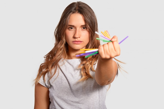 Atraente mulher séria detém amarrota palhas de plástico na mão, demonstra seu forte sentimento de viver em um planeta limpo