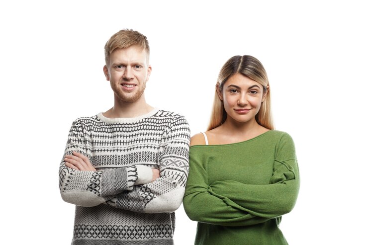 Foto grátis atraente sorridente jovem barbudo masculino e loira, vestindo suéteres elegantes, em pé ao lado do outro com os braços cruzados, sua aparência expressando confiança. pessoas, estilo de vida e relacionamentos