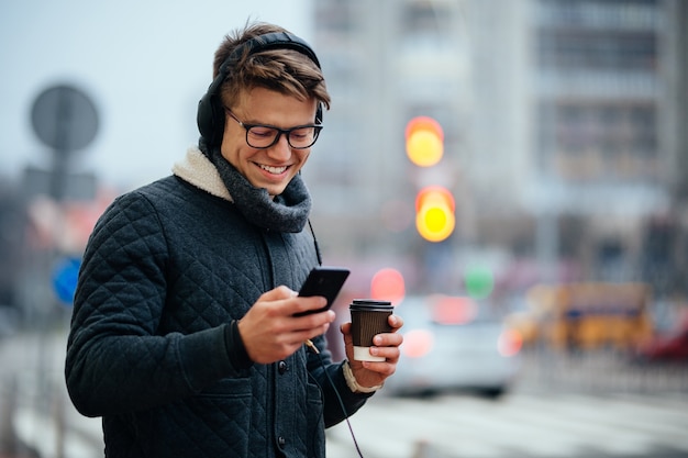 Atraente, sorrindo, sujeito, escutar música, em, fones, usando, seu, telefone móvel