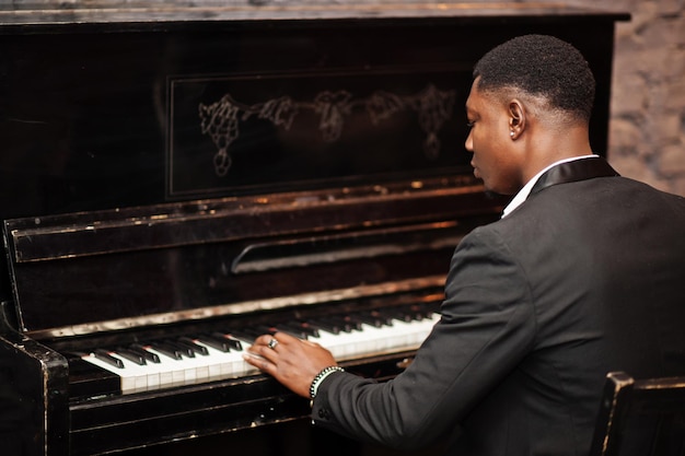 Atrás do forte e poderoso homem afro-americano de terno preto toca piano