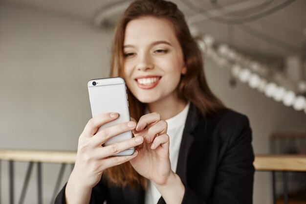 Atrativa senhora de escritório sentada em um café com um smartphone