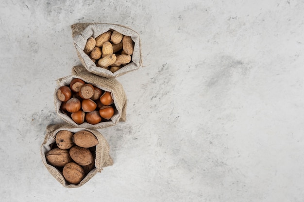 Avelãs com casca orgânicas, amendoim e nozes em saco na mesa de mármore.