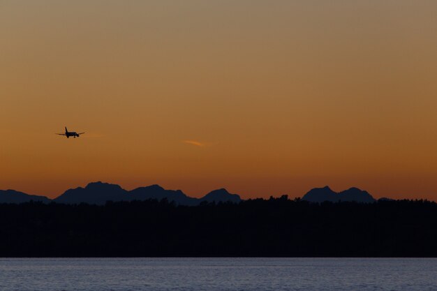 Avião voando sobre colinas e mar ao pôr do sol