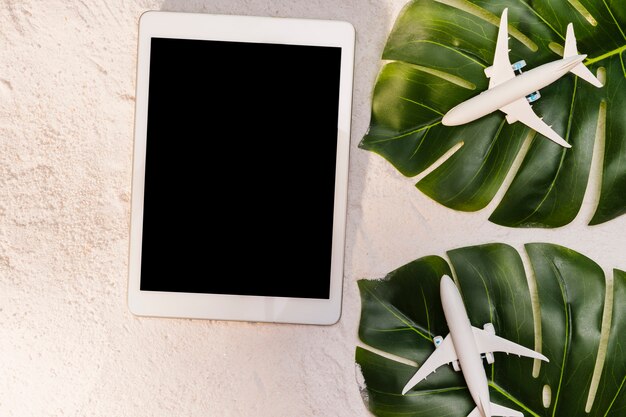 Aviões de brinquedo em folhas de monstera e tablet