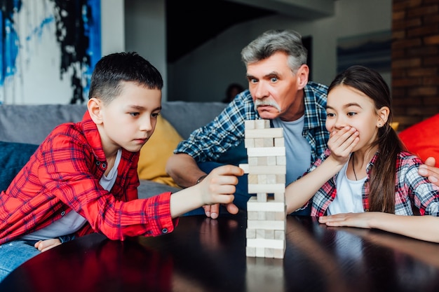Avô engraçado que joga o jogo de torre de madeira de blocos com filha e filho.