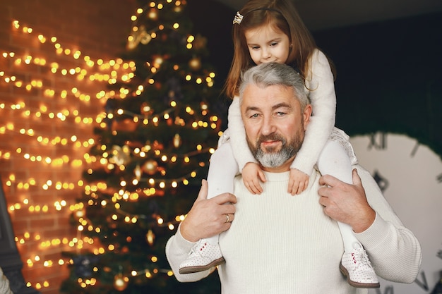 Avô sentado com sua neta. Comemorando o Natal em uma casa aconchegante. Homem com uma camisola de malha branca.