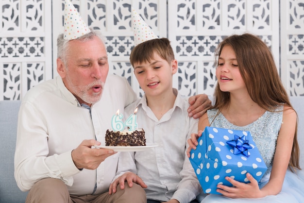 Avô, soprando a vela de aniversário com seus netos