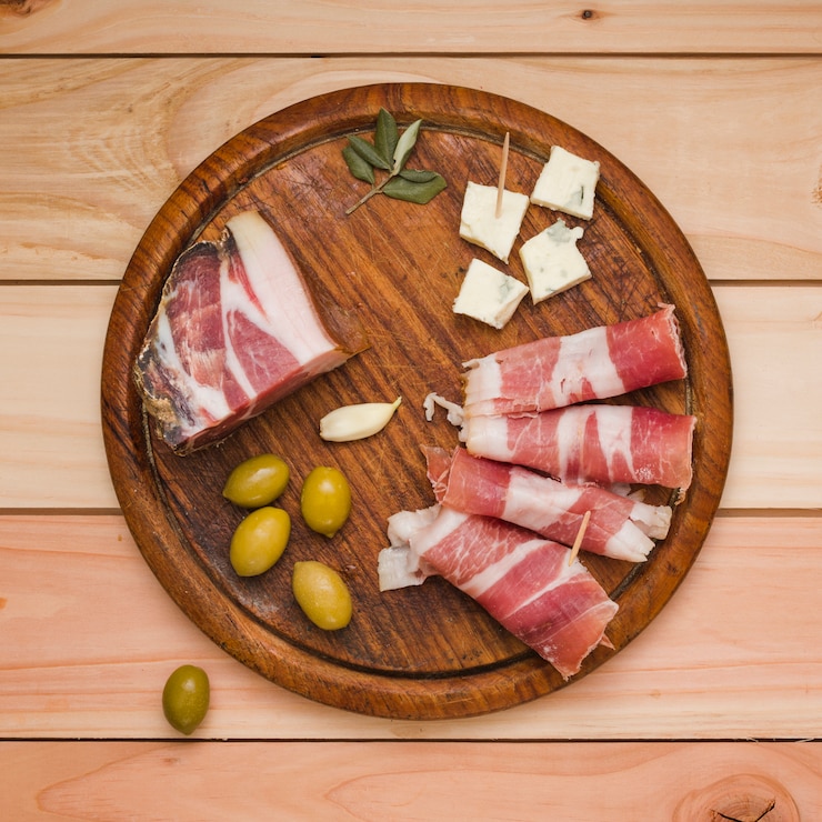Foto grátis azeitonas; dente de alho; fatia de queijo e bacon na bandeja de madeira sobre a mesa