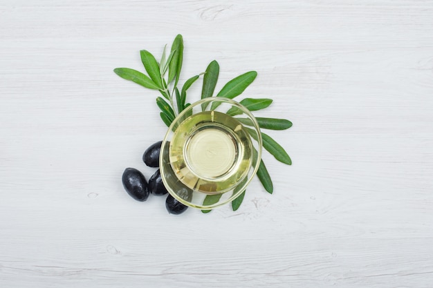 Azeitonas pretas e azeite de oliva em uma lata de vidro com folhas de oliveira vista superior na prancha de madeira branca