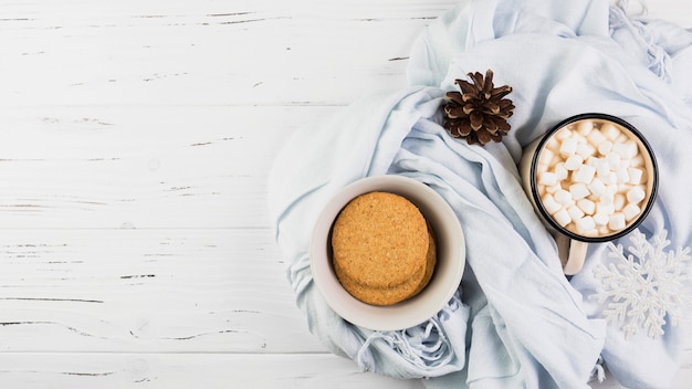 Bacia com biscoitos perto de copo com marshmallows e senão no lenço