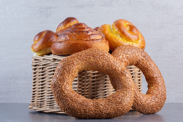 Bagels encostado em uma cesta cheia de pães doces em mármore.