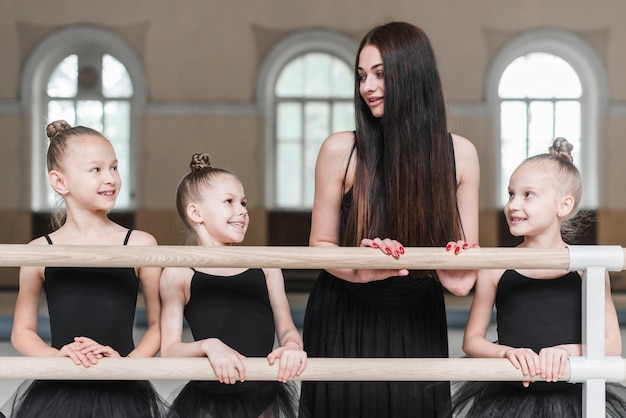 Bailarina meninas com o professor em pé atrás da barra na aula de dança