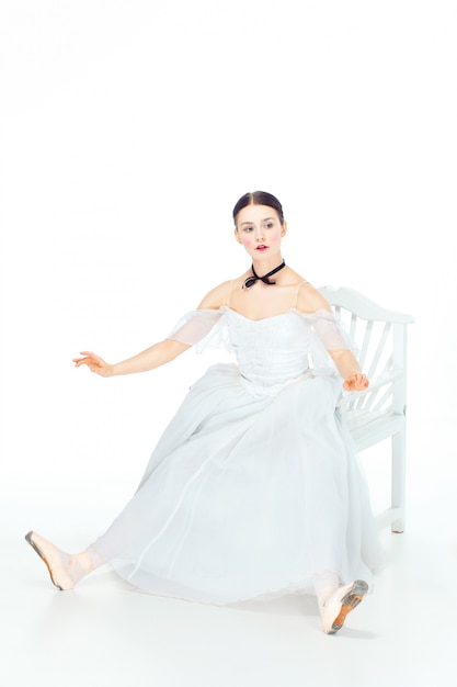 Bailarina no vestido branco sentado, espaço de estúdio.