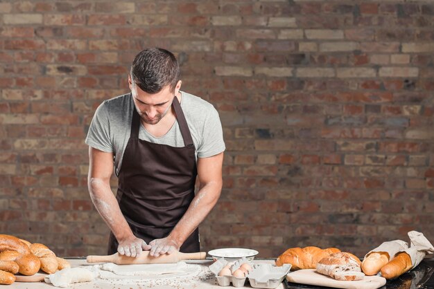 Baker, achatando a massa com o rolo no balcão contra a parede de tijolos