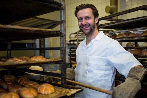 Baker mantendo a bandeja de pães assados ​​na prateleira