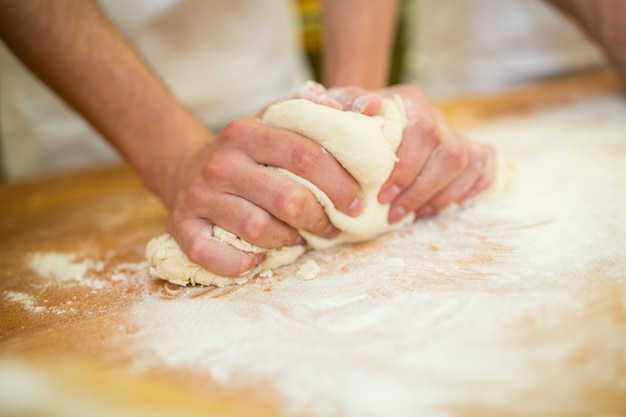 Bakers mãos amassam a massa no contador